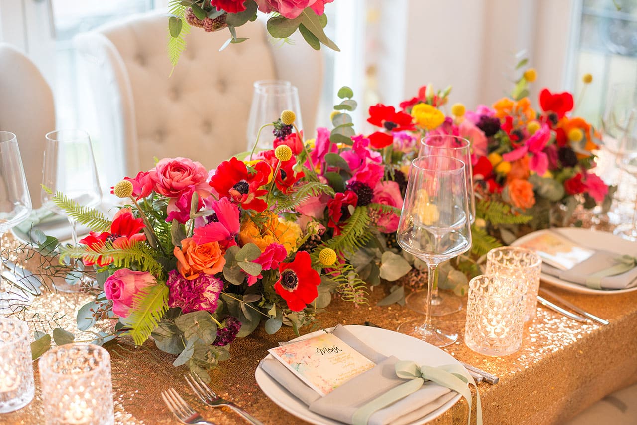 Tischdekoration mit Steckschaum aus bunten Blumen in Orange, Rot, Gelb und Pink